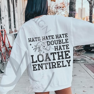 May include: White sweatshirt with a distressed finish, displaying a graphic on the back. The design features the words "HATE HATE HATE DOUBLE HATE LOATHE ENTIRELY" in black, alongside an illustration.