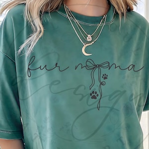 May include: Green t-shirt with the text "fur mama" in a cursive font, along with a bow and paw prints. The shirt has a crew neck and short sleeves. The word "HEART" is at the bottom of the shirt.