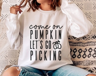 May include: White sweatshirt with the text "come on PUMPKIN let's go PICKING" in black. The sweatshirt is a crew neck style. The person in the image is wearing blue jeans.