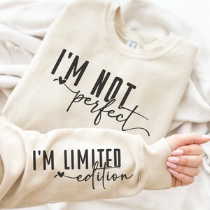 May include: A beige sweatshirt with the text "I'm not perfect I'm limited edition" printed on it.