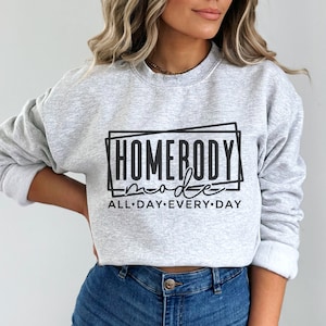 May include: Gray sweatshirt with black text that reads "Homebody mode all day every day" in a boxy font.