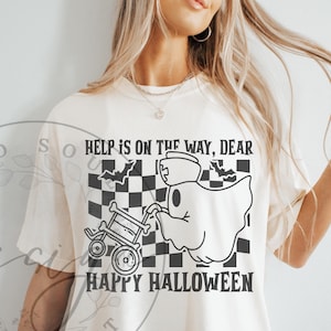 May include: Cream-colored t-shirt with a black and white Halloween graphic. The design features a ghost pushing a skeleton cart, bats, and a checkered background. Text reads "HELP IS ON THE WAY, DEAR" and "HAPPY HALLOWEEN."