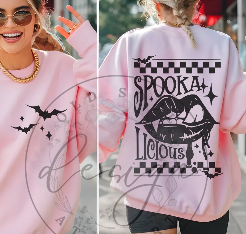 May include: A light pink sweatshirt with black bat and star graphics on the front. The back features the words "Spookalicious" with a vampire mouth graphic, bats, and a checkered pattern. A casual Halloween-themed top.