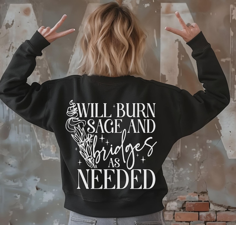 May include: Black sweatshirt with white text that reads "Will burn sage and bridges as needed". The text is accompanied by a stylized image of a burning sage bundle.
