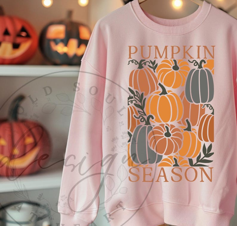May include: A light pink sweatshirt featuring a graphic of various pumpkins in shades of orange, gray, and brown. The words "PUMPKIN SEASON" are printed in a decorative font, perfect for autumn.