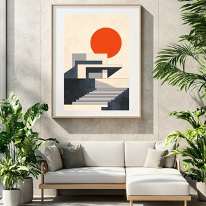 Puede incluir: Una impresión artística enmarcada que presenta un diseño arquitectónico abstracto con un gran sol rojo. La obra de arte muestra un edificio moderno con escaleras, en tonos de gris, beige y negro. La impresión se muestra sobre un sofá blanco.