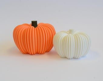 Könnte beinhalten: Zwei dekorative Kürbisse. Einer ist orange mit einem dunkelgrünen Stiel, der andere ist weiß. Beide haben vertikale Rippendetails. Diese herbstlichen Dekorationen sind perfekt für saisonale Ausstellungen.