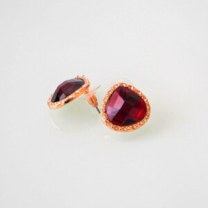 May include: A pair of gold-tone earrings with a red gemstone set in a clear crystal halo.