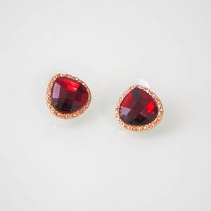 May include: A pair of red gemstone earrings with a gold setting and a clear crystal border.