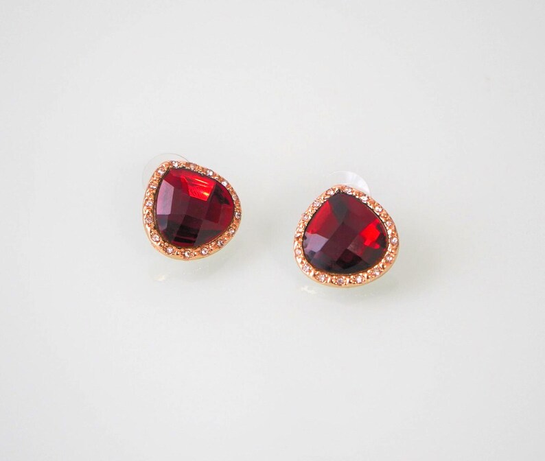 May include: A pair of red gemstone earrings with a gold setting and a clear crystal border.