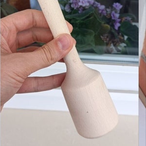 May include: A wooden potato masher with a light brown handle and a slightly wider, rounded base. The handle has two dark brown bands.