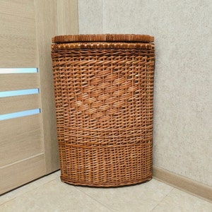 Pode incluir: Uma cesta de roupa de vime castanho com tampa. A cesta é tecida com um padrão de linhas horizontais e verticais.