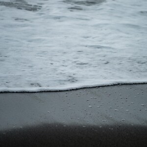 Puede incluir: Fotografía en escala de grises de una escena de playa. La imagen captura el encuentro del océano y la orilla. La parte superior muestra las olas oceánicas blancas y espumosas, mientras que la parte inferior revela la arena oscura y húmeda. La línea del horizonte es visible.