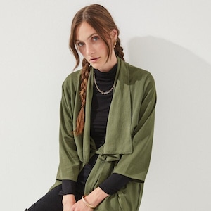 May include: A long, olive green, belted cardigan with a shawl collar. The cardigan is made of a soft, flowing fabric and has a relaxed fit.