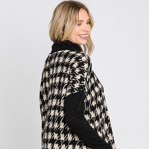 May include: Black and cream houndstooth patterned sweater with a mock neck and long sleeves. The sweater has a side slit and a black ribbed hem.