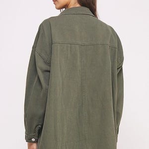 以下が含まれることがあります： オリーブグリーンのボタンダウンシャツジャケット。クラシックな襟、ボタン付きカフスの長袖、バックヨーク、背中中央を縦に走る縫い目が特徴です。この衣服は、目に見えるステッチが施された質感のある生地で作られています。