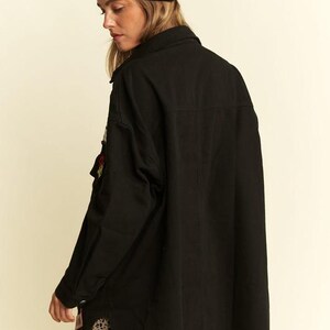 以下が含まれることがあります： 黒いビーニーと、襟と胸ポケットに小さな刺繍パッチが付いた黒い長袖のボタンダウンシャツ。シャツは裾がカーブしたデザインで、黒いヒョウ柄のタンカラーのスカートの上に着用されています。