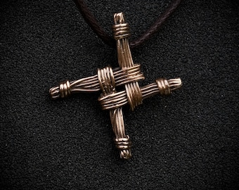 Puede incluir: Un collar con un colgante de nudo celta de bronce con un diseño tejido. El colgante está en un cordón de cuero marrón.