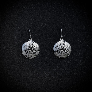 May include: A pair of silver earrings with a circular design featuring four stylized animal figures. The earrings are hanging from a black background.