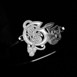 May include: A silver Celtic knot bracelet with a detailed design. The knot is in the shape of a letter G.
