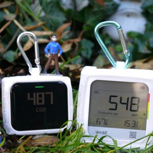 Könnte beinhalten: Zwei weiße Luftqualitätsmonitore mit digitalen Displays, die CO2-Werte anzeigen. Der Monitor links zeigt einen Wert von 487 ppm an, der Monitor rechts einen Wert von 548 ppm. Beide Monitore haben einen Karabinerhaken.