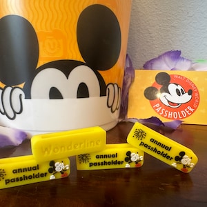 May include: Three yellow plastic Mickey Mouse themed keychains. One keychain says "Wonderline" and the other two say "annual passholder" with a firework graphic and a Mickey Mouse silhouette.