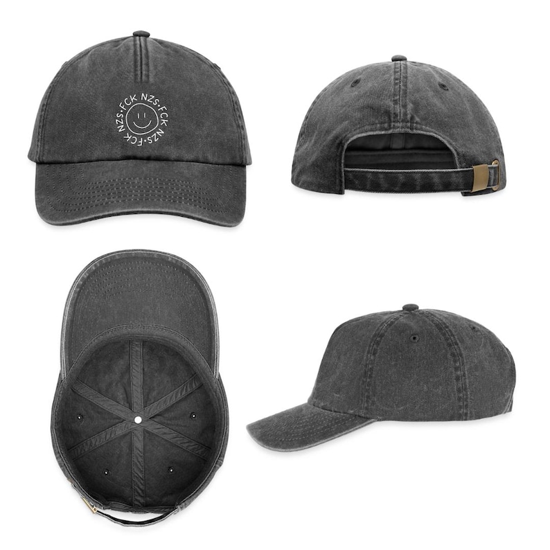May include: A charcoal gray baseball cap with a distressed finish, featuring a white circular graphic on the front panel containing a smiley face and the text NZS.FCK. The cap includes a curved brim, eyelets, and an adjustable metal buckle strap.