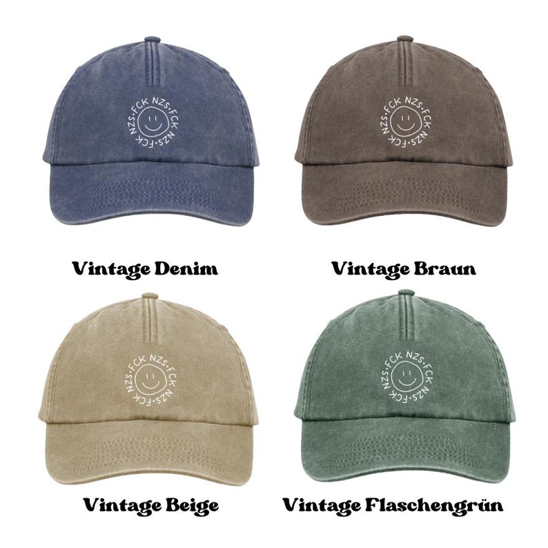 May include: Four baseball caps in vintage denim blue, brown, beige, and bottle green. Each cap features a centered white embroidered circular design with a smiley face and the text FCK NZS repeated around the perimeter of the circle.
