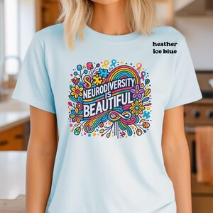 May include: A light blue t-shirt with a colorful graphic design that says "Neurodiversity is Beautiful". The graphic features flowers, a rainbow, and a puzzle piece.