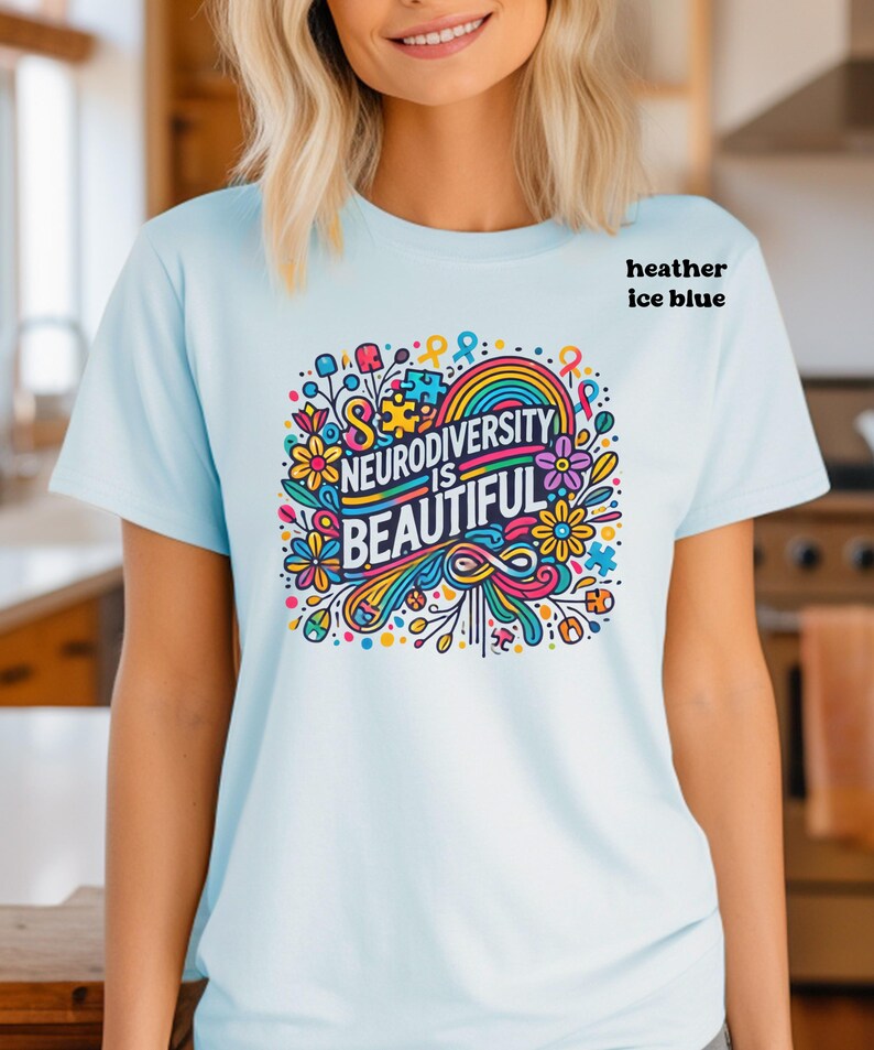 May include: A light blue t-shirt with a colorful graphic design that says "Neurodiversity is Beautiful". The graphic features flowers, a rainbow, and a puzzle piece.