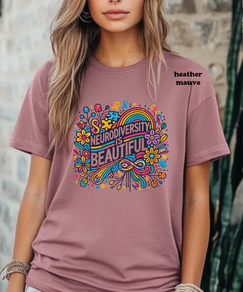 Neurodiversity is beautiful is shown through the print and is the colour of the shirt. It is outlined in black. On this heather mauve shirt, vibrant flowers, autism symbols and puzzle pieces surround the words.