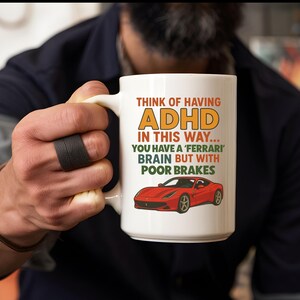 Peut inclure: Mug en céramique blanche avec le texte "THINK OF HAVING ADHD IN THIS WAY... YOU HAVE A 'FERRARI' BRAIN BUT WITH POOR BRAKES" et une illustration d'une voiture de sport rouge. Le mug est tenu par une personne.