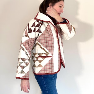 Könnte beinhalten: Gesteppte Jacke mit Patchwork-Design. Sie hat eine Mischung aus rotem Karomuster, Weiß und gemustertem Stoff. Die Jacke hat einen weißen Kragen, rote Paspeln und Knopfverschlüsse. Sie wird mit einer blauen Jeans getragen.