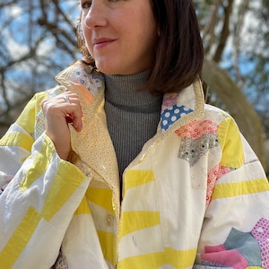 Könnte beinhalten: Patchwork-Jacke mit einer Vielzahl von Stoffmustern und Farben, darunter Gelb, Weiß und Pastelltöne. Die Jacke hat einen Kragen und eine Knopfleiste. Das Design erinnert an einen Vintage-Quilt.