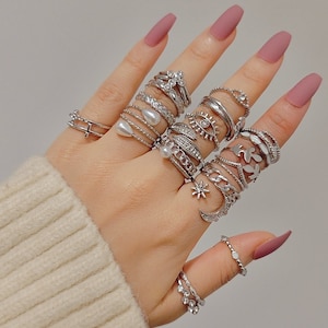 Puede incluir: Un maniquí de mano con una variedad de anillos de plata, incluyendo un anillo de perla, un anillo de ojo y un anillo con un diseño de estrella.