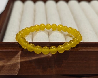 May include: A yellow beaded bracelet resting on a wooden jewelry box. The bracelet is made of small, round, translucent beads. The text "AVATHING 2024 production" is visible in the image.