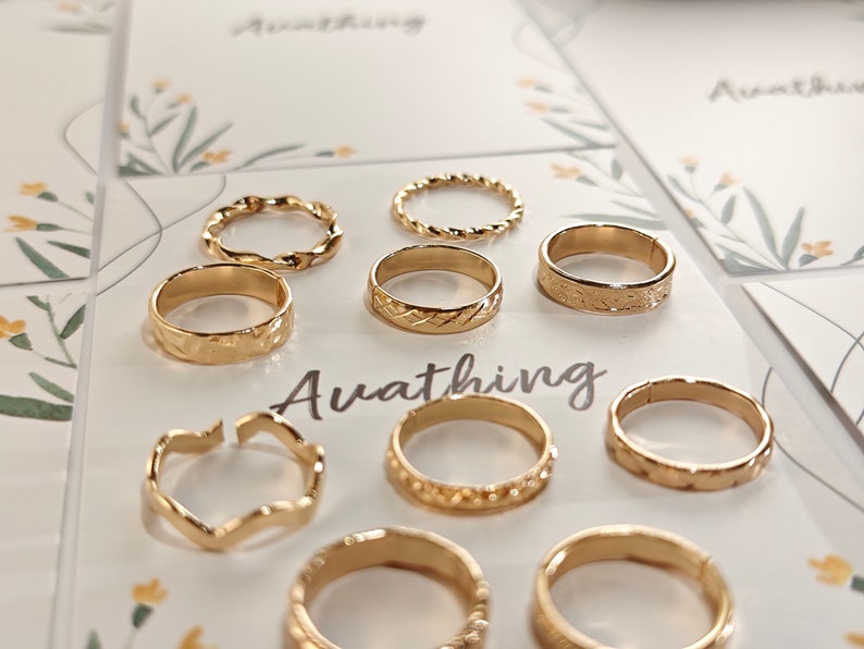 May include: A set of nine gold-toned rings with different designs, including twisted, textured, and open-work styles. The rings are displayed on a white background with the word "Awathing" printed in black.