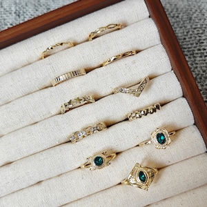 May include: A set of ten gold rings with green gemstones. The rings are displayed in a wooden box with a white fabric lining.