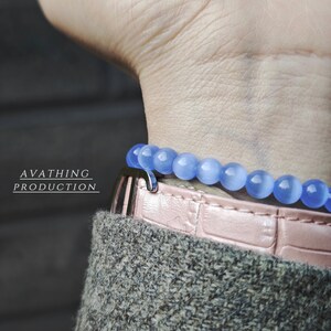 May include: A light blue beaded bracelet with a silver clasp on a pink leather wristband. The bracelet is on a person's wrist.