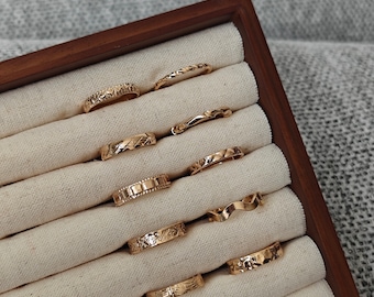 May include: A set of ten gold-toned rings with different textured designs, displayed in a wooden ring box with beige fabric lining.