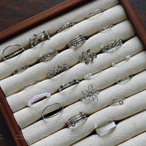 May include: A set of 20 silver rings in a wooden box with white fabric lining. The rings are various styles, including simple bands, chain links, and floral designs.
