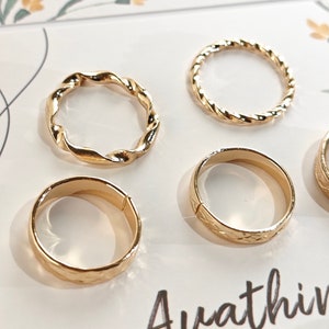 May include: Set of six gold-toned rings with different designs. The rings are arranged on a white background with the word "Avathin" printed on the bottom right corner.