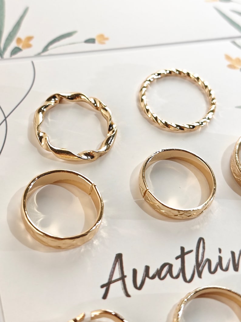 May include: Set of six gold-toned rings with different designs. The rings are arranged on a white background with the word "Avathin" printed on the bottom right corner.