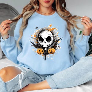 Puede incluir: Sudadera azul claro con un dise&ntilde;o de Jack Skellington de Pesadilla antes de Navidad. El dise&ntilde;o incluye una calavera blanca, detalles negros y dos calabazas naranjas, ideal para Halloween.