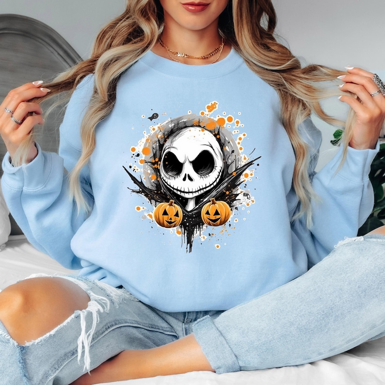 Puede incluir: Sudadera azul claro con un dise&ntilde;o de Jack Skellington de Pesadilla antes de Navidad. El dise&ntilde;o incluye una calavera blanca, detalles negros y dos calabazas naranjas, ideal para Halloween.