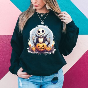 May include: Black sweatshirt featuring a Halloween-themed graphic. The design includes a skeleton figure, pumpkins, and candles. The skeleton is in a black suit and is set against a light blue background. The pumpkins are orange and the candles are yellow.