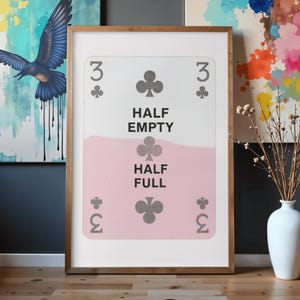 Puede incluir: Una impresión de arte mural rectangular enmarcada con un diseño de carta de juego estilizada. La carta muestra el número 3, símbolos de trébol y el texto "HALF EMPTY" sobre una línea de relleno horizontal rosa claro, con "HALF FULL" debajo.