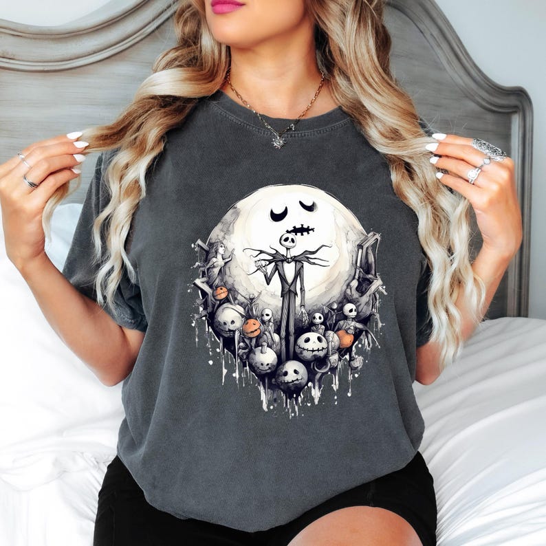 Puede incluir: Camiseta gris oscuro con un gr&aacute;fico de Jack Skellington de The Nightmare Before Christmas. El dise&ntilde;o incluye una luna llena, varios personajes y un efecto de salpicadura. La camiseta es de cuello redondo y tiene mangas cortas.
