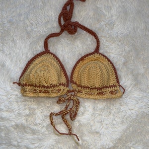 May include: A crocheted bikini top with brown and beige yarn. The top has a halter style with a tie at the back and a tie at the front.
