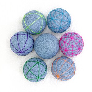 Puede incluir: Siete bolas de hilo grises con diseños de cuerda de diferentes colores. Las bolas están dispuestas en círculo sobre un fondo blanco.